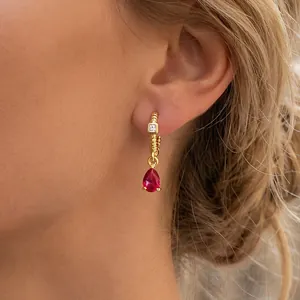 Detailed view of 18K gold huggie earring with pear-cut red zircon and textured spiral finish