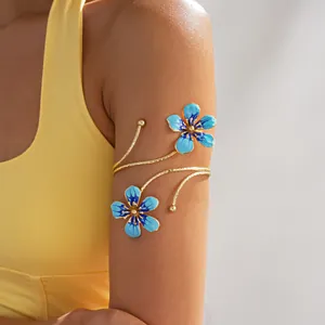 Close-up of a gold arm cuff with blue enameled flowers on a model