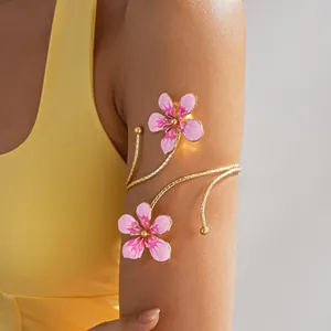 Detailed view of a gold-toned flower arm cuff with pink enamel petals on a model's arm.