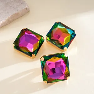 Primer plano de tres cristales cuadrados de arco iris en monturas doradas sobre piedra beige.