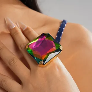 Primer plano de un anillo con una gran gema cuadrada multicolor en una banda dorada.