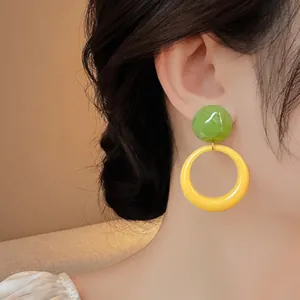 Close-up view of a green and yellow resin hoop earring on a model ear.