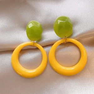Close-up of vibrant green and yellow resin hoop earrings on champagne satin.