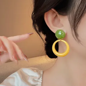Close-up detail of forest style green and yellow resin circular drop earrings on a model