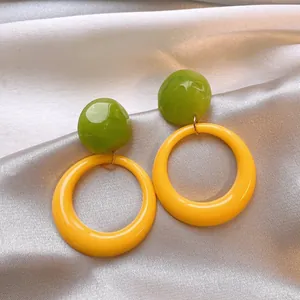 Detailed macro view of vibrant green and yellow resin hoop earrings on soft silk cloth