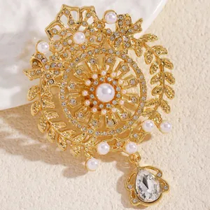 Dettaglio di una spilla dorata stile lusso con perle e ciondolo a goccia di cristallo.
