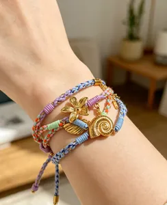 Détail de bracelets bohèmes tissés avec breloques coquillages et fleurs dorées au poignet
