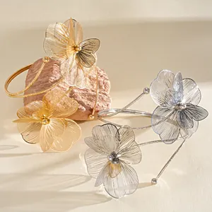 Close-up detail of elegant gold and silver metal flower petal open arm cuffs on natural stone.