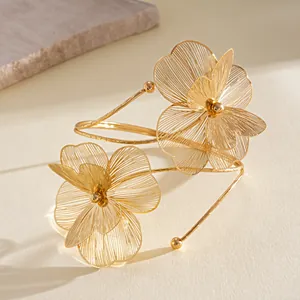Macro view of gold metal open arm cuff with intricate filigree flower petals