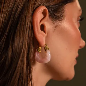 Detailed close-up of a pink marbled resin and 18k gold U-shaped earring worn on a model's ear