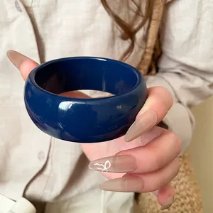 Primo piano di un ampio braccialetto in resina blu scuro lucido tenuto in mano su lino