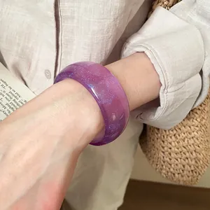 Primo piano di un grosso bracciale rigido in resina viola con sottili glitter blu
