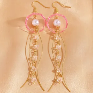Gros plan de boucles d'oreilles méduses roses élégantes avec fils dorés et perles sur satin