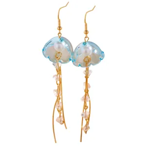 Vue détaillée de ces boucles d'oreilles méduses en résine bleu clair et dorées.