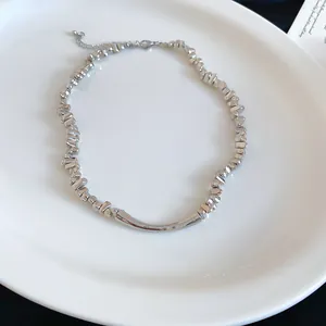 Close-up van zilveren ketting met onregelmatige metalen kralen en een gebogen staaf.