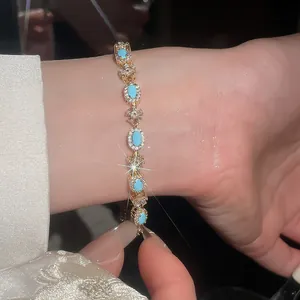 Primo piano di un bracciale dorato con resina turchese e cristalli indossato al polso.
