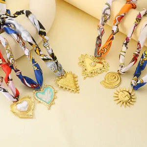 Dettaglio di girocollo in seta bohémien con pendenti a forma di sole e cuore dorati