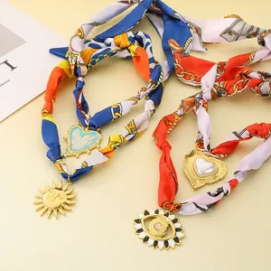 Dettaglio di girocollo in sciarpa di seta vintage con pendenti a sole e cuore dorati.