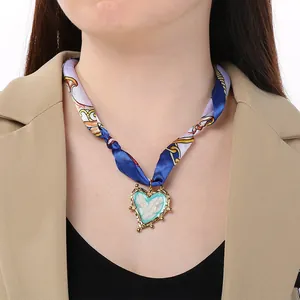 Dettaglio ravvicinato del choker in foulard di seta retrò con ciondolo a cuore smaltato