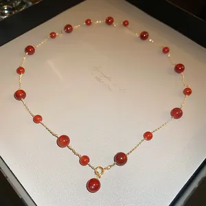 Dettaglio di una collana dorata con perle di vetro rosse in una confezione regalo.
