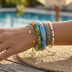 Detailed close-up of stacked resin tube bracelets, pearl beads, and gold shell charms