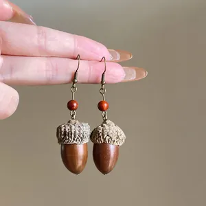 Detailed view of handmade acorn drop earrings with red bead and vintage hooks