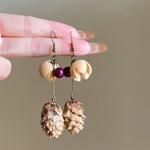 Detailed close-up of vintage ethnic earrings with pinecone pendants held by hand