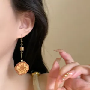 A detailed close-up showing a vintage metallic pinecone pendant earring on an ear.