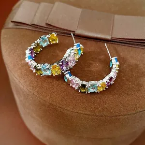Silver needle hoop earrings with colorful oval zircon stones on a brown jewelry box