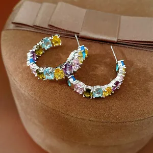Close-up of colorful oval cubic zirconia C-shaped hoop earrings on a velvet box.