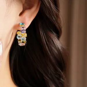 Close-up detail of vibrant oval zircon hoop earrings with silver needles on ear.