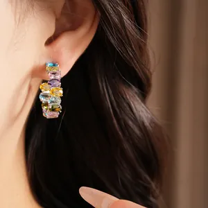 Close-up detail of luxury colorful oval zircon hoop earrings worn on an ear, elegant style