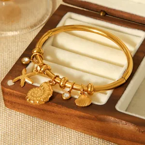 Macro detail of 18K gold plated stainless steel bangle with starfish and shell charms