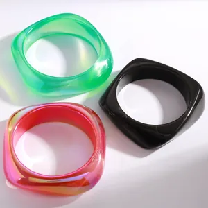 Nahaufnahme von drei klobigen geometrischen Harz-Armreifen in Grün, Pink und Schwarz auf Weiß