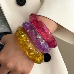 Nahaufnahme von drei bunten Harzarmbändern mit Goldfolie am Handgelenk eines Models