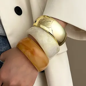 Gestapelte grobe Harz- und Goldmetall-Armreifen in Bernstein und Creme am Handgelenk