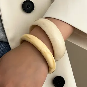 Detail von creme- und elfenbeinfarbenen Resin-Armreifen mit marmorierter Textur am Handgelenk