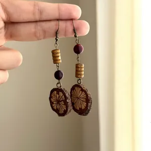 Detailed view of handmade ethnic Maillard style beaded wood slice dangle earrings held by hand.