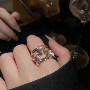 Detail of a vintage gold open ring featuring three pink heart crystals worn on index finger