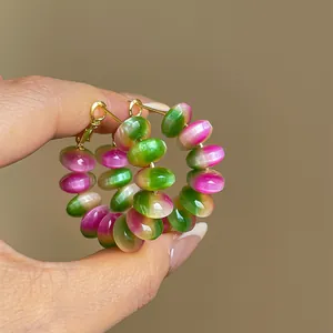 Close-up of pink and green gradient resin beaded hoop earrings held by hand