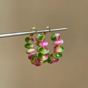 Close-up view of vibrant rainbow gradient resin beaded hoop earrings on a metal stand.