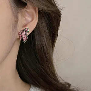 Elegant colorful butterfly stud earrings with pink and green stones on a model's ear