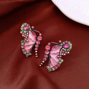 Vintage butterfly stud earrings with pink and green rhinestones on brown silk texture.