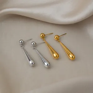 Gros plan d'élégantes boucles d'oreilles gouttes en acier doré et argenté sur soie.