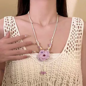 Primo piano di una collana con ciondolo a fiore lavorata a maglia viola su una modella