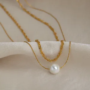Gros plan d'un collier élégant à double chaîne dorée avec une perle blanche unique.