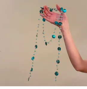 Detailed shot of a bohemian blue-green shell necklace held by hand against a tan background