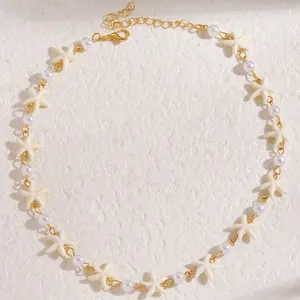 Dettaglio della collana dorata a strati con ciondoli a stella marina e piccole perle bianche