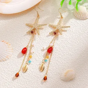 Détail de boucles d'oreilles à franges avec étoile de mer dorée, perles et coquillages