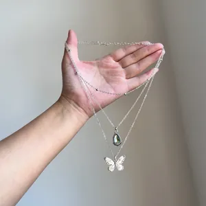 Hand-held view of vintage layered necklace featuring resin teardrop and butterfly pendants